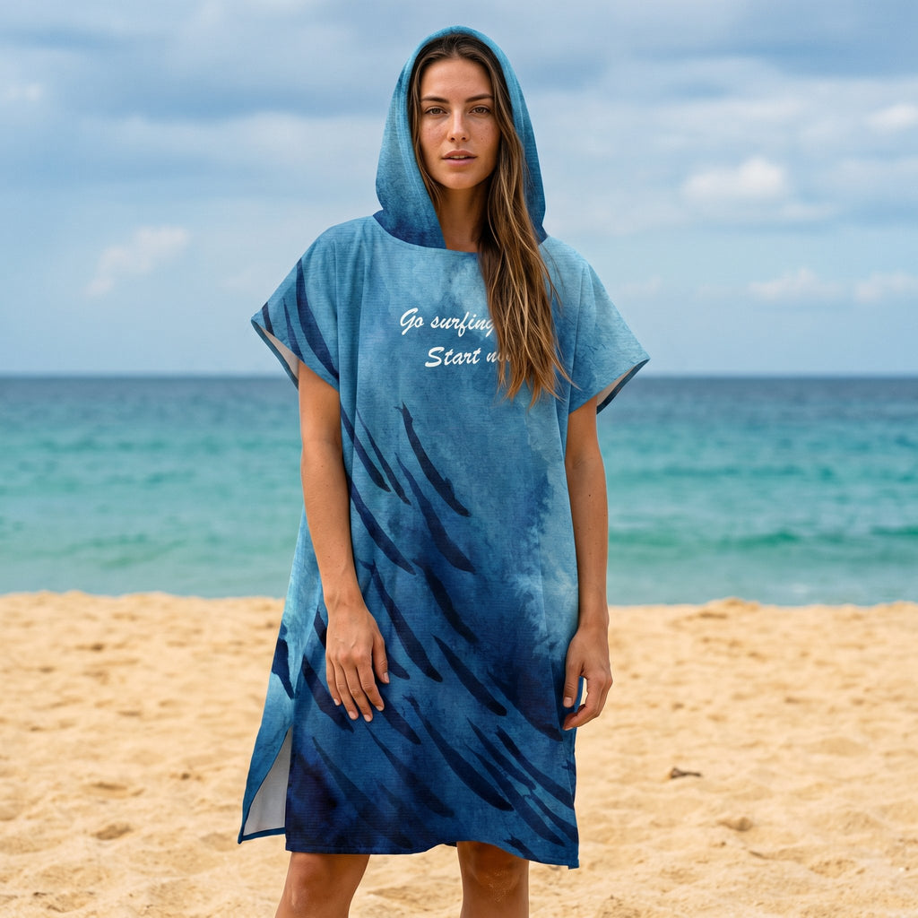 Poncho serviette à capuche motif baleine et lune, porté par une femme debout sur la plage, le poncho visible en entier.