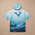 Poncho serviette à capuche motif dauphin turquoise, posé à plat sur un fond uni beige.