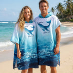 Poncho serviette à capuche motif dauphin turquoise, porté par un couple souriant debout sur une plage de sable fin.
