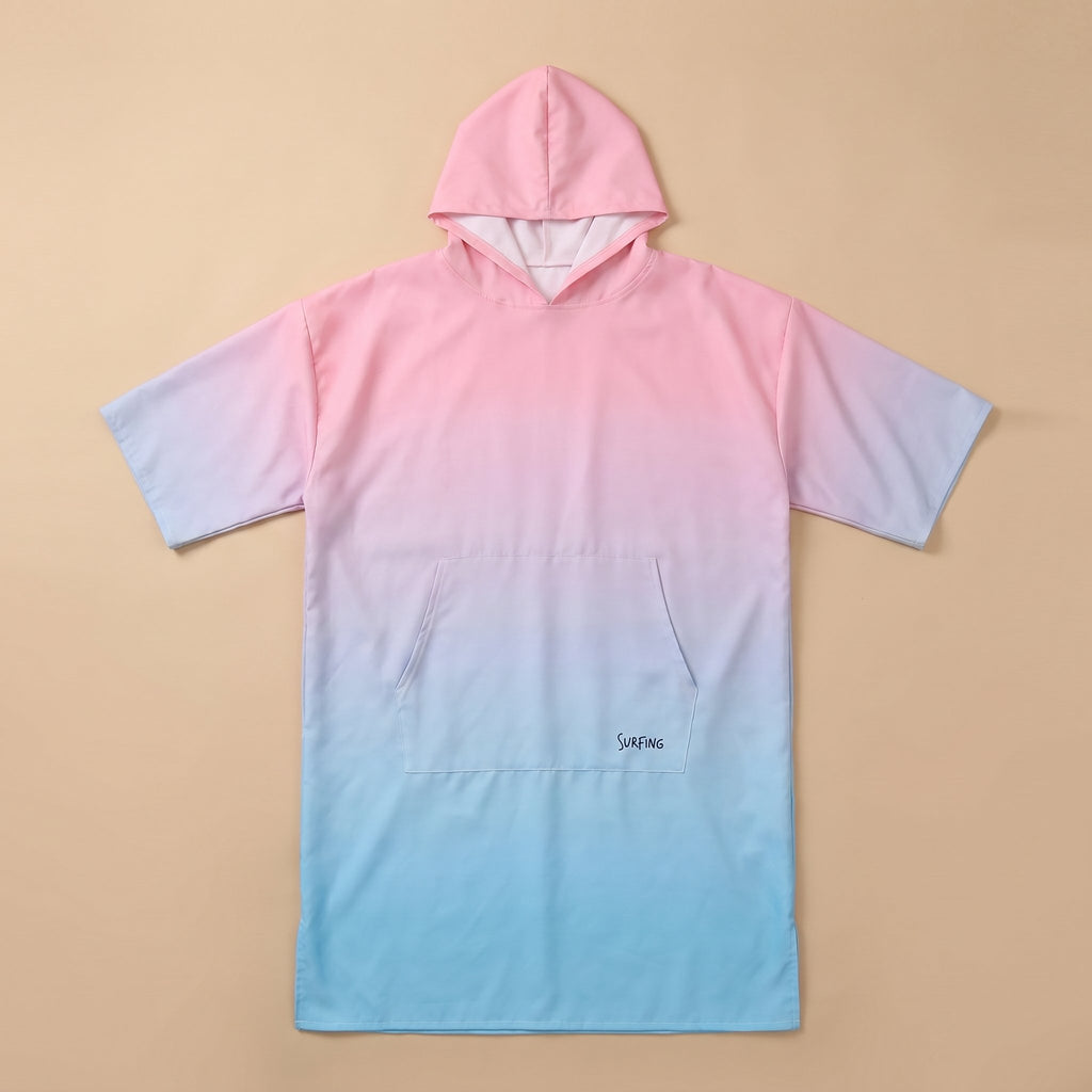 Poncho serviette à capuche dégradé rose et bleu, posé à plat sur un fond beige clair.
