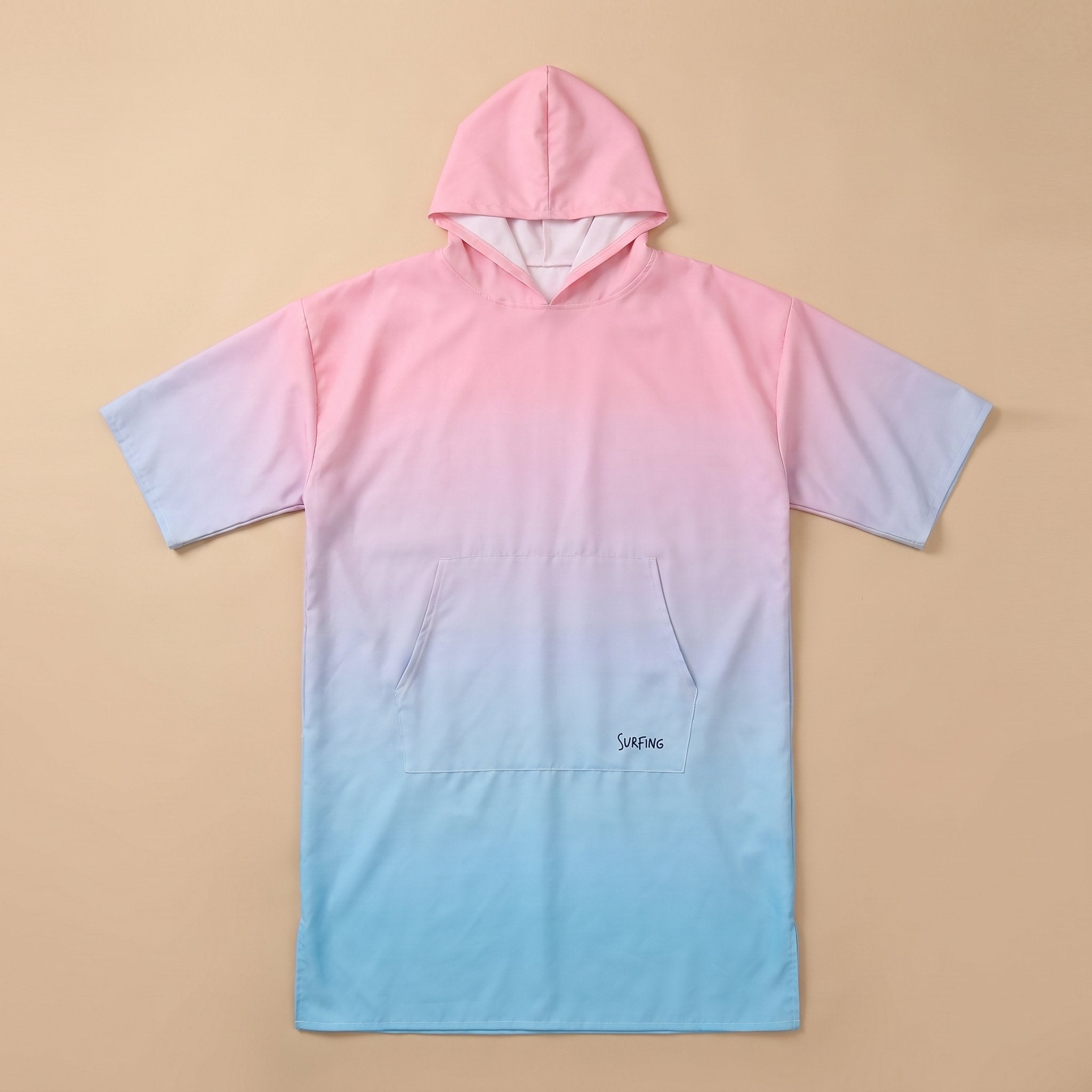 Poncho serviette à capuche dégradé rose et bleu, posé à plat sur un fond beige clair.