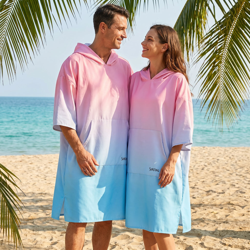Poncho serviette à capuche dégradé rose et bleu, porté par un homme et une femme se regardant sur une plage ensoleillée.