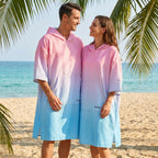 Poncho serviette à capuche dégradé rose et bleu, porté par un homme et une femme se regardant sur une plage ensoleillée.