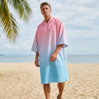 Poncho serviette à capuche dégradé rose et bleu, porté par un homme debout sur la plage, regardant vers l'avant.