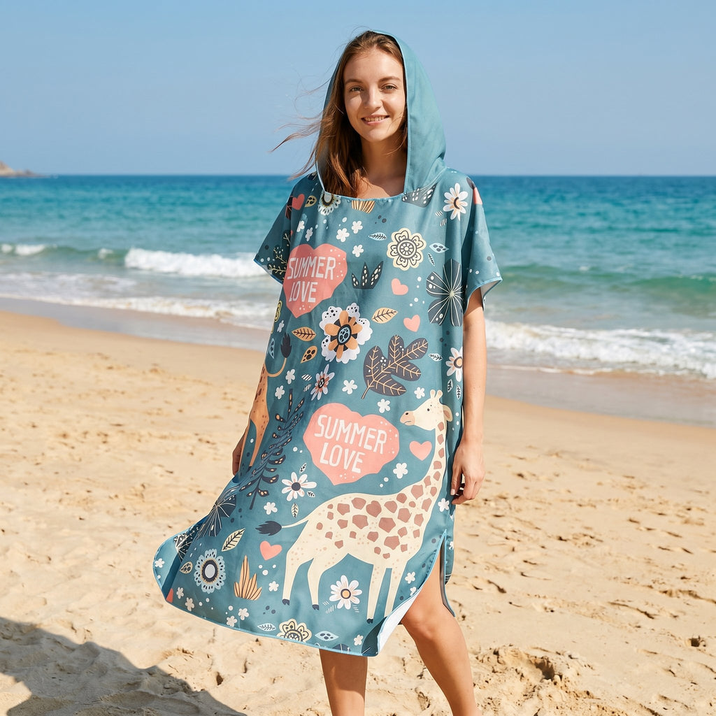 Poncho serviette a capuche motif girafes d'été porté par une femme debout sur la plage, souriante.