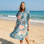 Poncho serviette a capuche motif girafes d'été porté par une femme debout sur la plage, souriante.