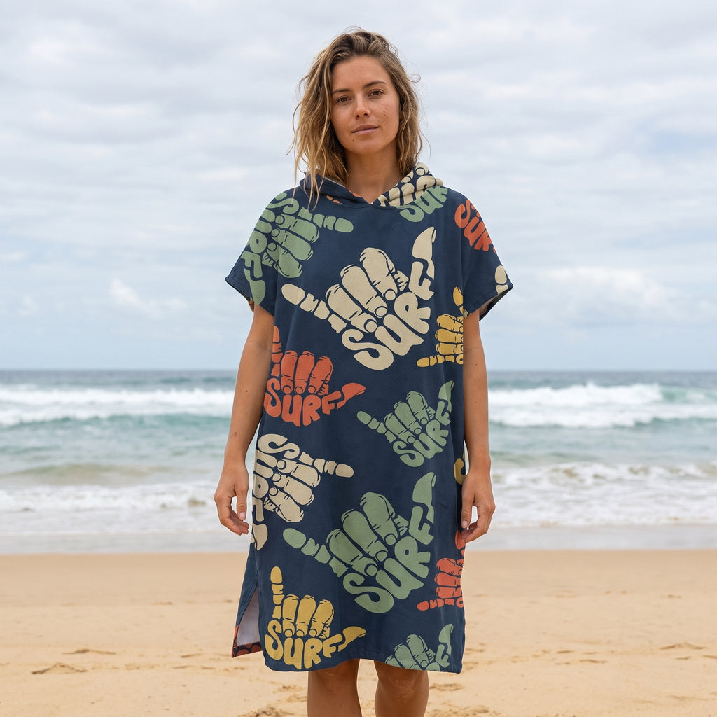 Poncho serviette à capuche motif shakas colorés, porté par une femme de face sur une plage de sable.