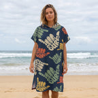 Poncho serviette à capuche motif shakas colorés, porté par une femme de face sur une plage de sable.