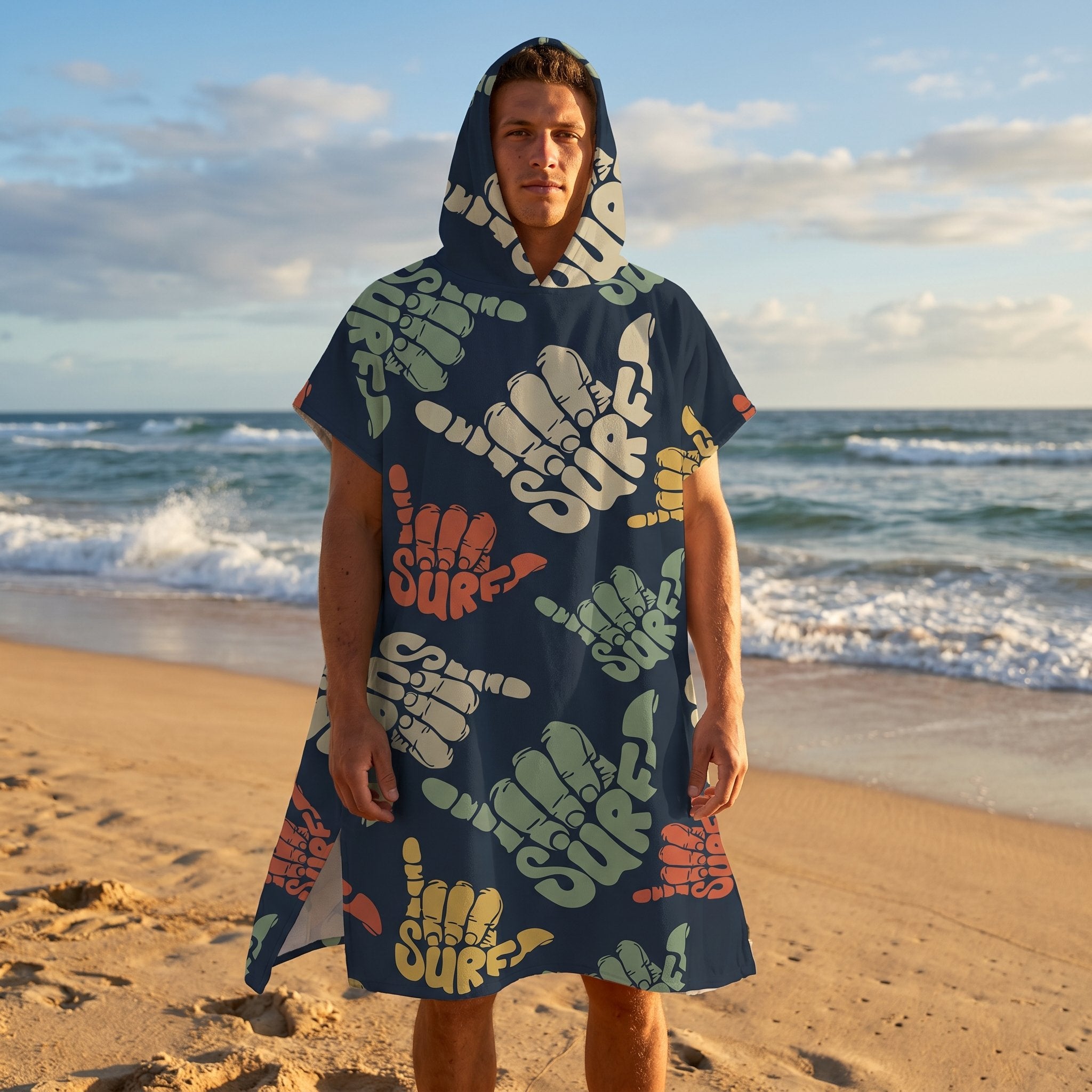 Poncho serviette à capuche motif shakas colorés, porté par un homme de face, les bras le long du corps sur la plage.