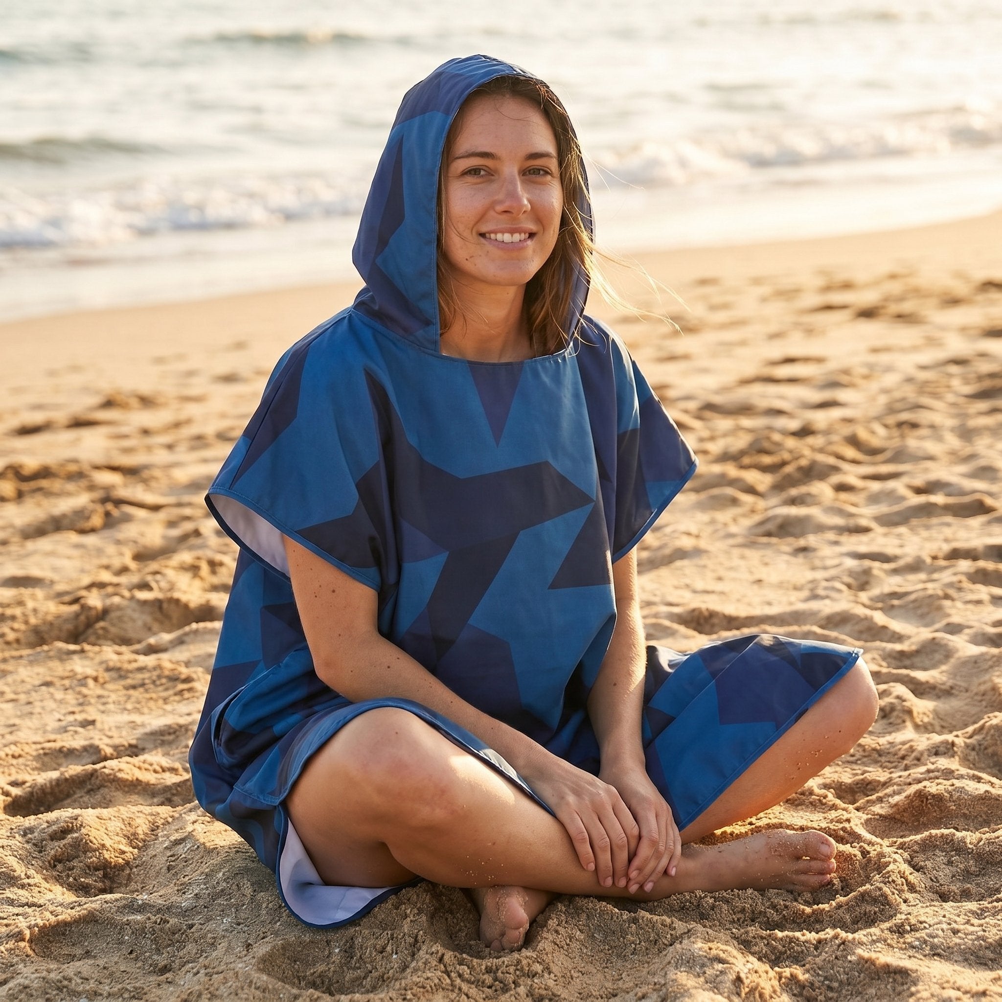 Poncho de surf à capuche · Triangles, porté par une femme assise sur le sable, regardant vers l'avant.