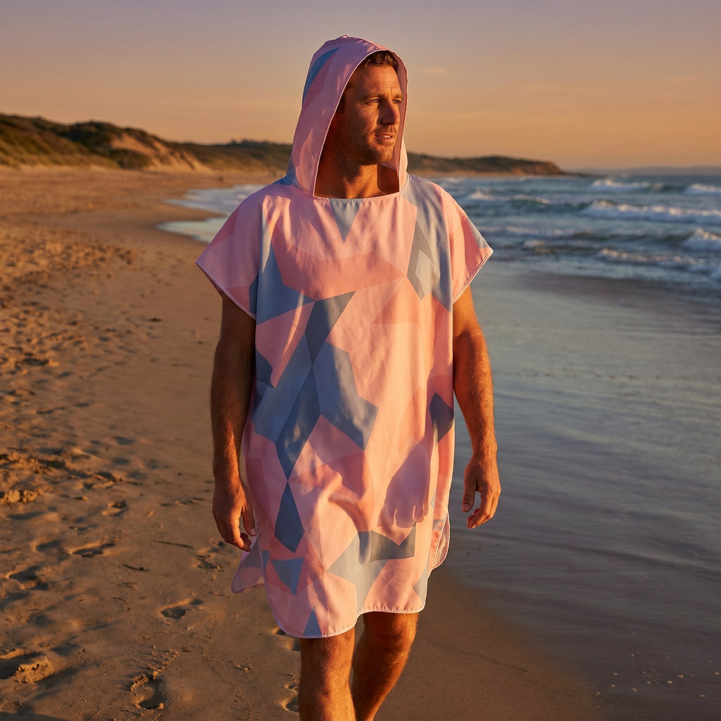 Poncho de surf à capuche · Triangles, porté par un homme marchant sur la plage au coucher du soleil, vu de trois quarts face.