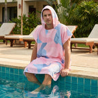 Poncho de surf à capuche · Triangles, porté par un homme assis au bord d'une piscine, les pieds dans l'eau.