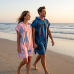 Deux ponchos de surf à capuche · Triangles, portés par un couple marchant main dans la main sur la plage, vus de face.