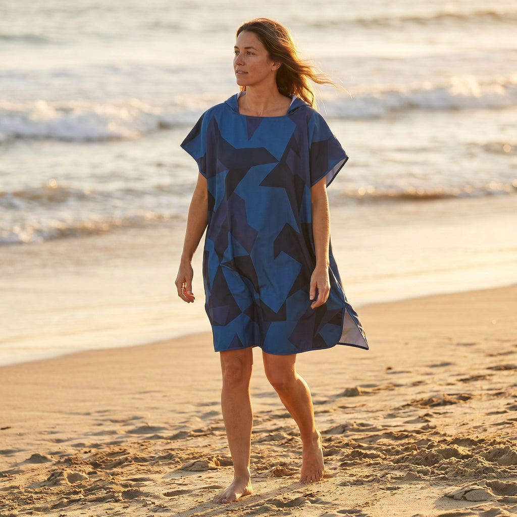 Poncho de surf à capuche · Triangles, porté par une femme marchant sur la plage, vue de profil, avec l'océan en arrière-plan.