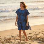 Poncho de surf à capuche · Triangles, porté par une femme marchant sur la plage, vue de profil, avec l'océan en arrière-plan.