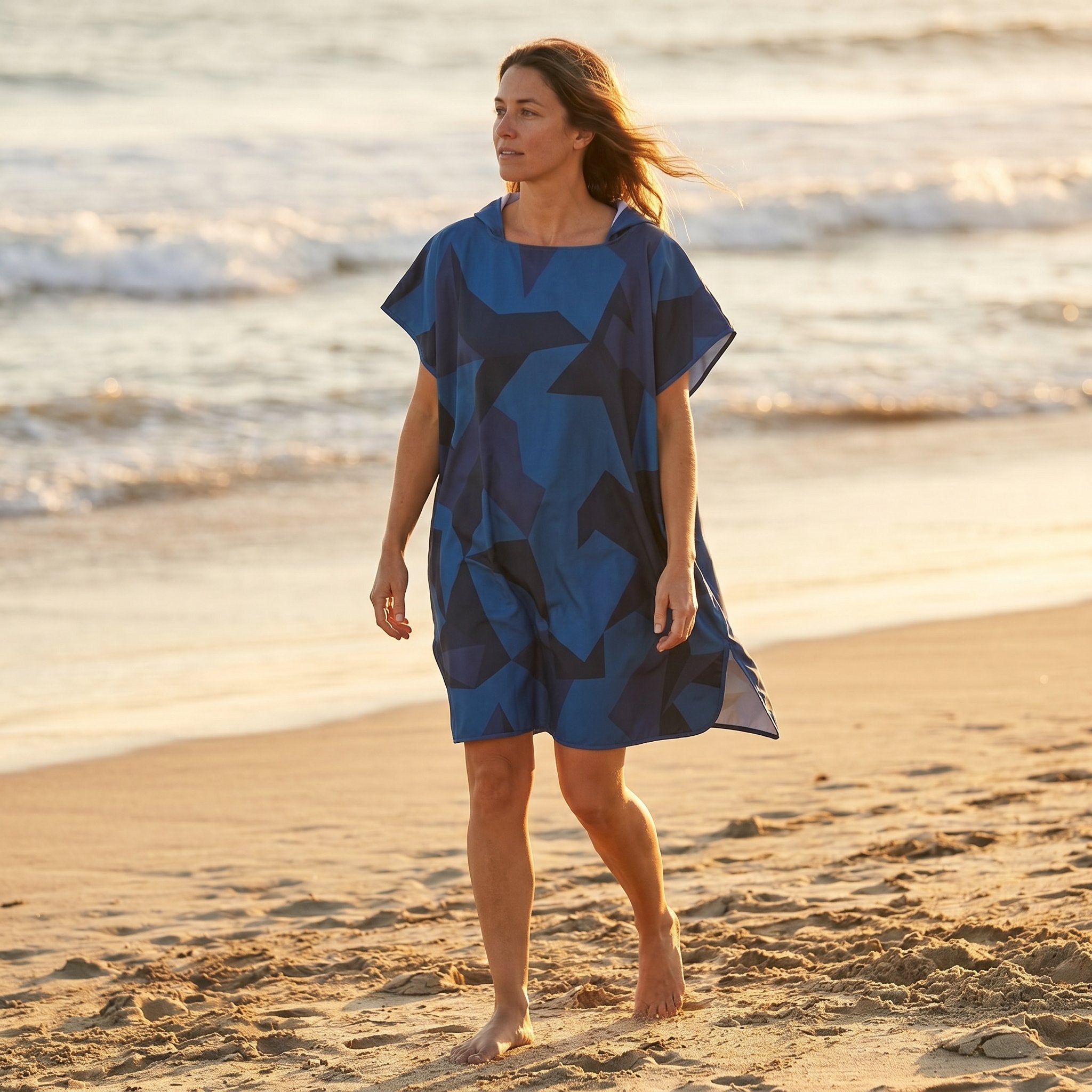 Poncho de surf à capuche · Triangles, porté par une femme marchant sur la plage, vue de profil, avec l'océan en arrière-plan.