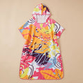 Poncho serviette a capuche motif tropical rose et jaune, posé à plat sur un fond beige clair.