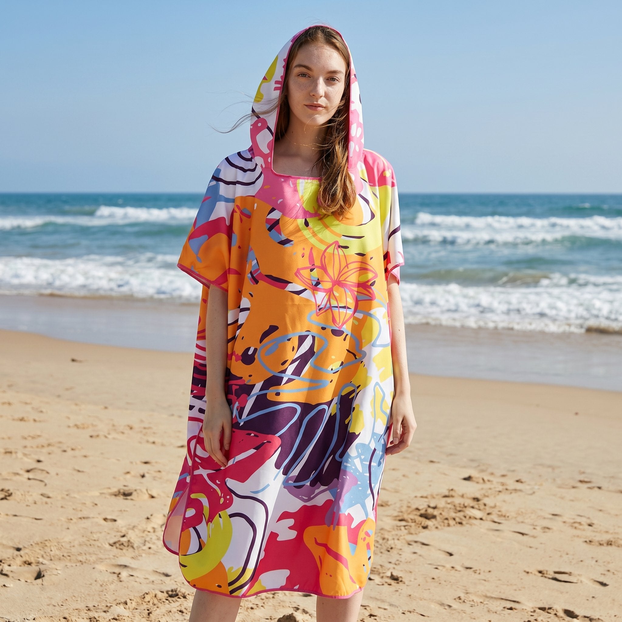 Poncho serviette a capuche motif tropical rose et jaune, porté par une femme debout face à l'océan.