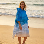 Poncho serviette à capuche motif vague océan, porté par une femme sur la plage.