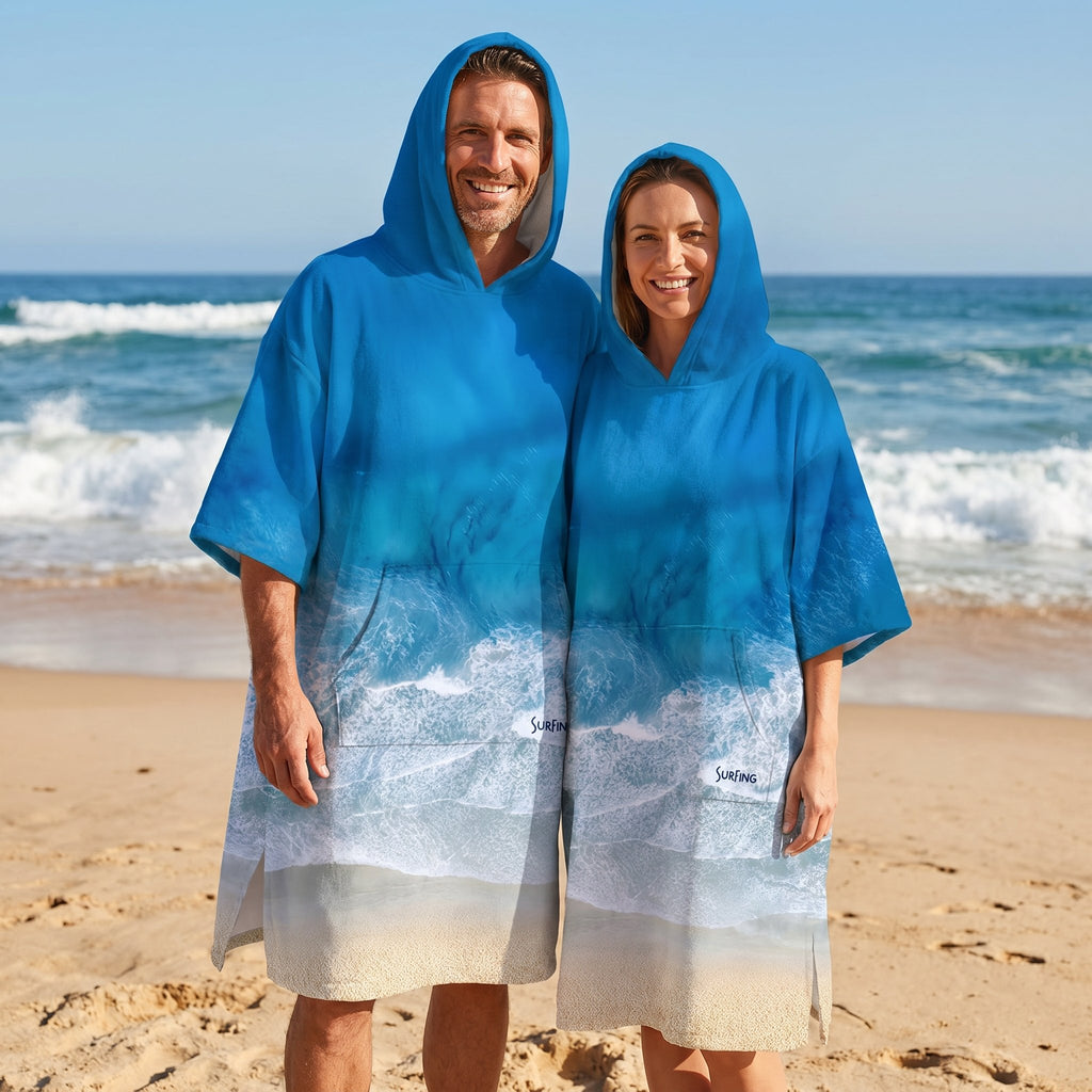 Poncho serviette à capuche motif vague océan, porté par un homme et une femme sur la plage.