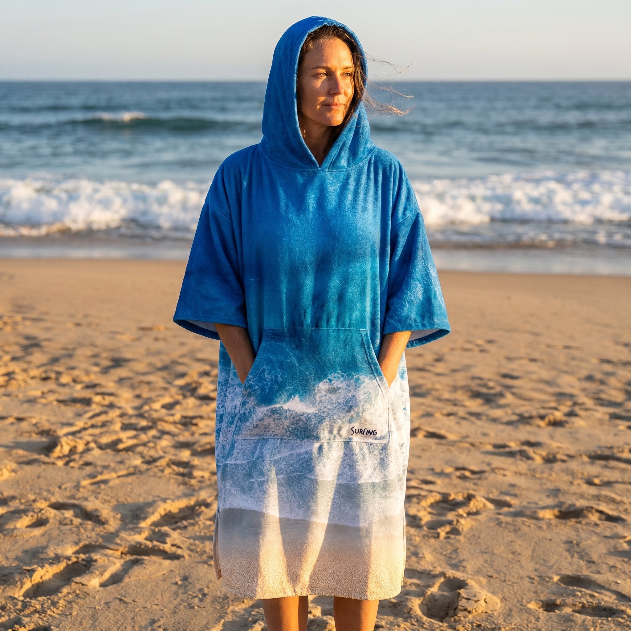 Poncho serviette à capuche motif vague océan, porté par une femme les mains dans les poches.