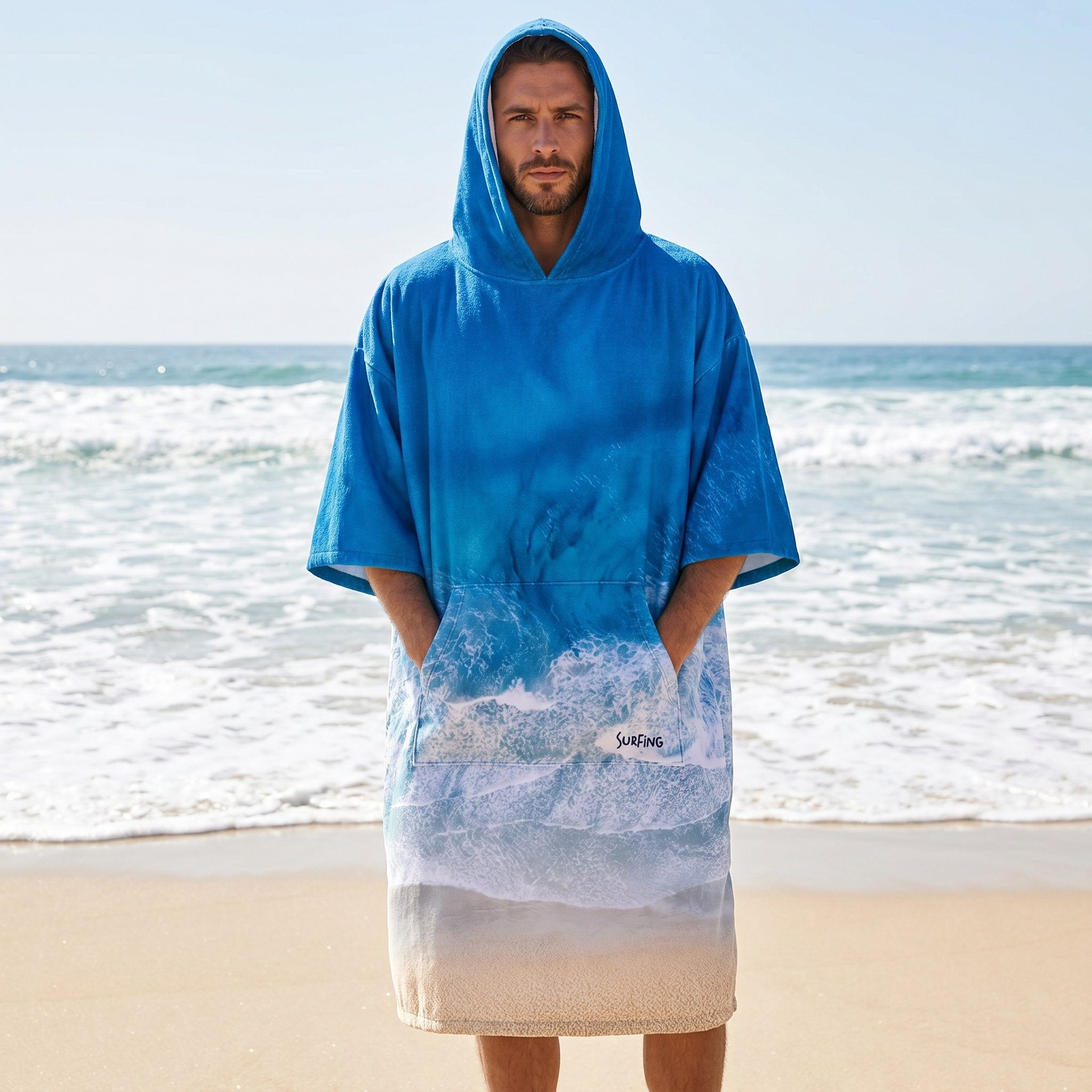 Poncho serviette à capuche motif vague océan, porté par un homme debout sur la plage.