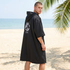 Poncho serviette à capuche noir uni, porté de dos par un homme, révélant un motif de vague sur le dos.