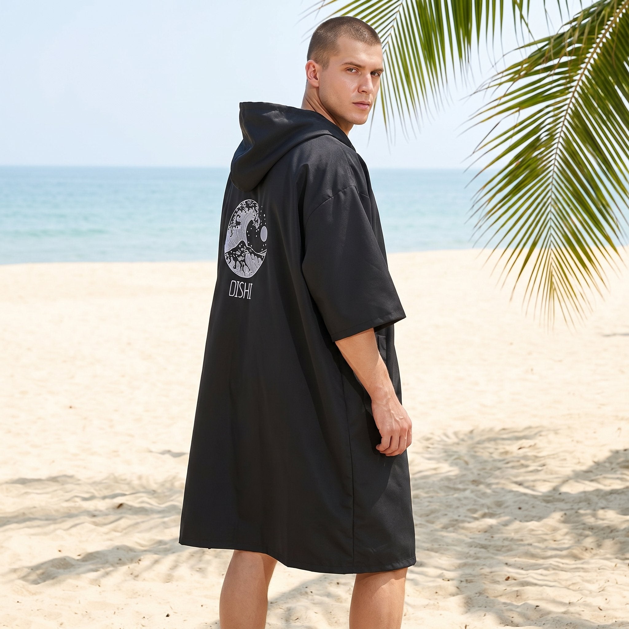 Poncho serviette à capuche noir uni, porté de dos par un homme, révélant un motif de vague sur le dos.