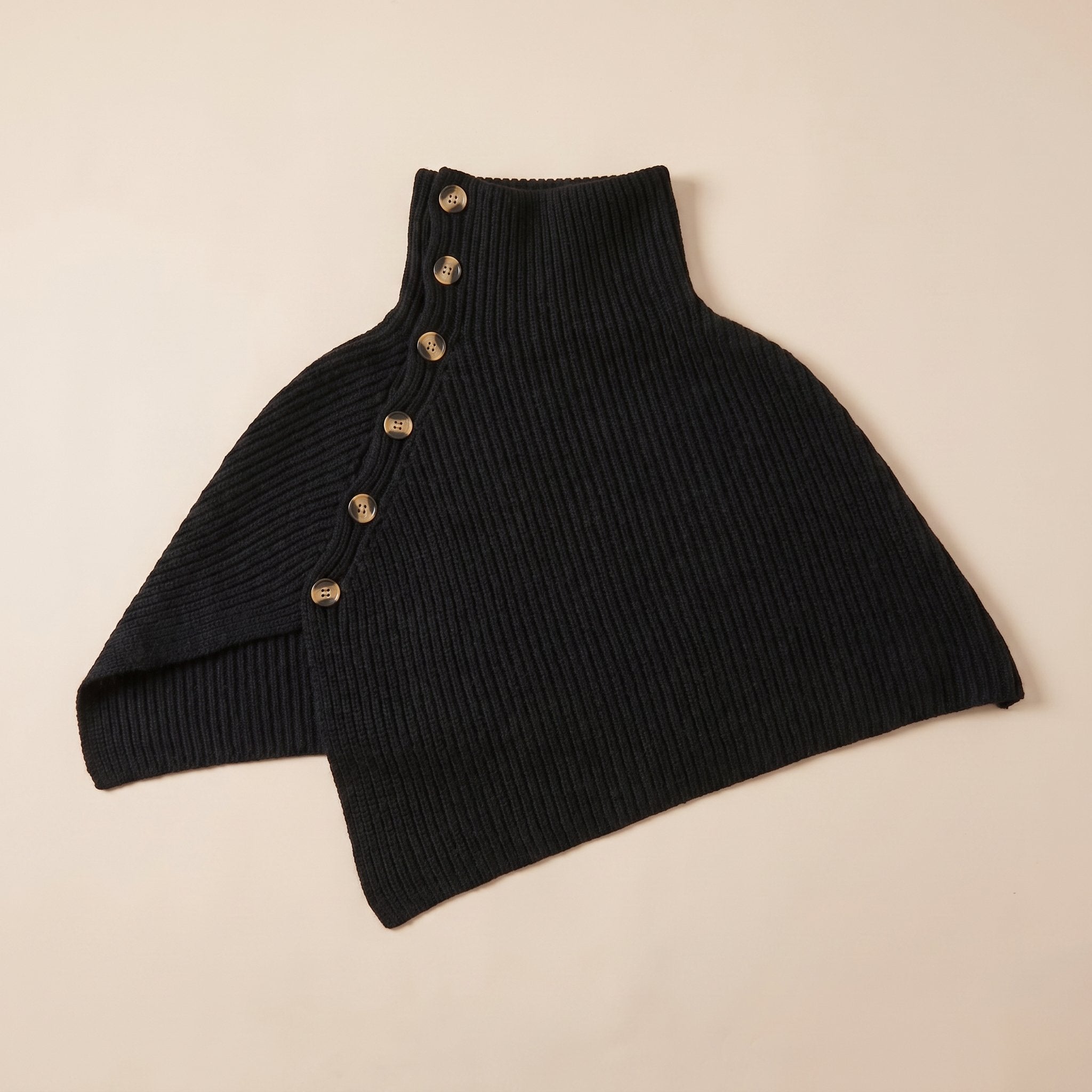 Poncho en laine femme noir, avec col montant et boutons, posé à plat sur un fond clair.