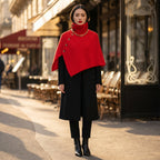 Poncho en laine femme rouge, porté par une femme debout de face devant une terrasse de café ensoleillée.