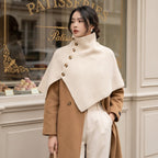Poncho en laine femme crème, porté par une femme de profil devant la vitrine d'une pâtisserie.