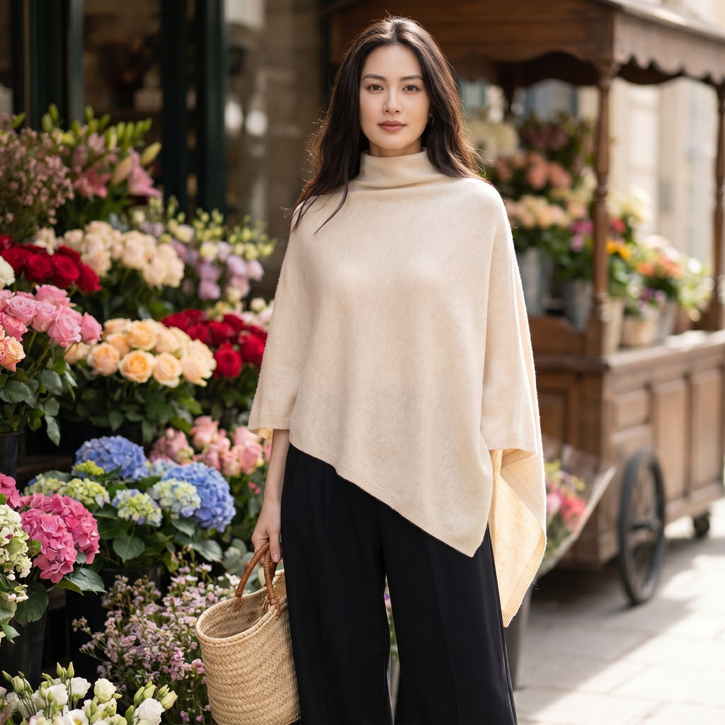 Poncho en laine femme col roulé crème porté par une femme, devant un étalage de fleurs colorées.