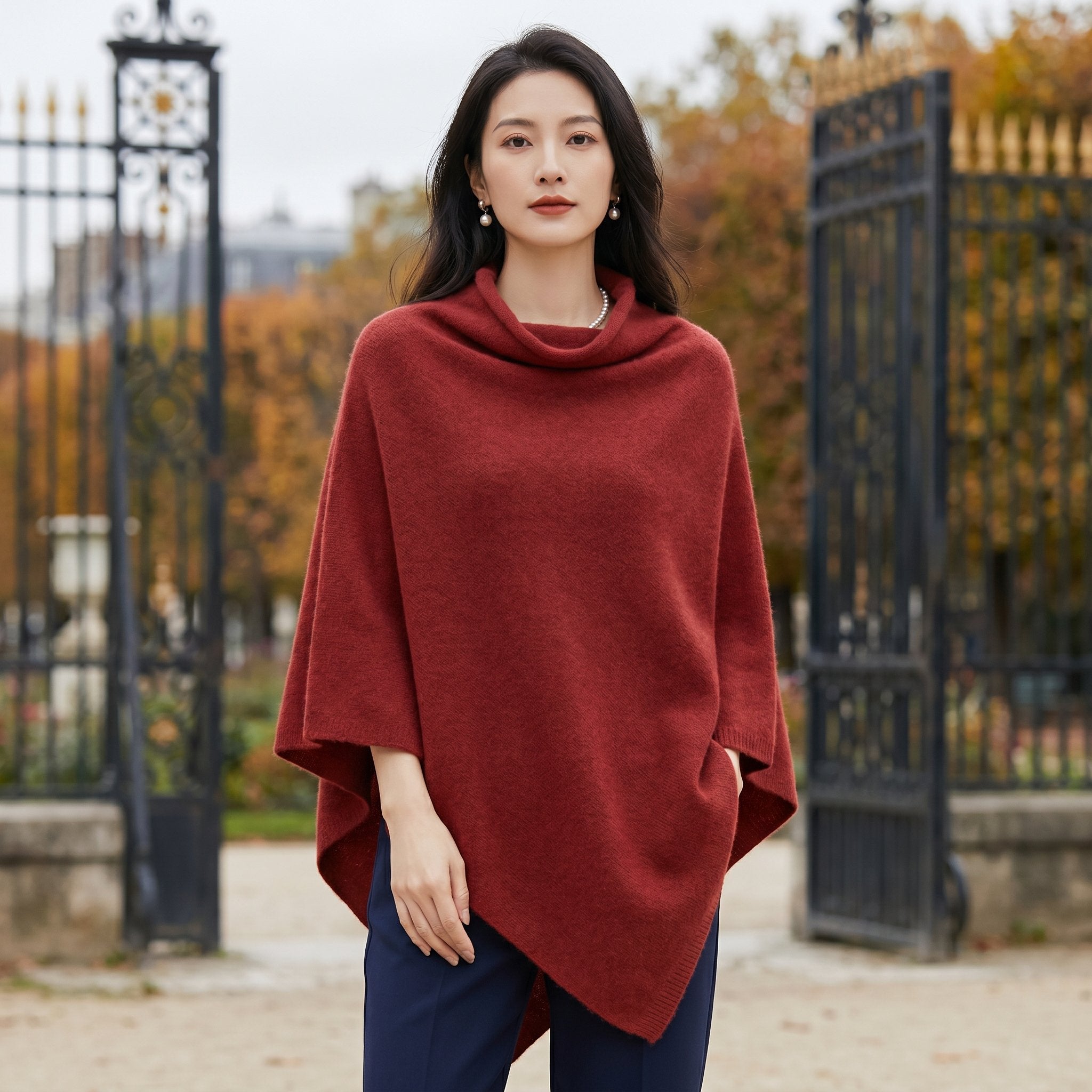 Poncho en laine femme col roulé rouge bordeaux porté par une femme, devant un portail de parc.