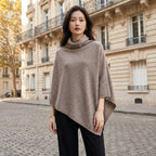 Poncho en laine femme col roulé taupe porté par une femme, en pied dans une rue pavée.
