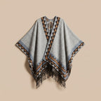 Poncho femme chaud à motif aztèque et franges gris clair, avec motifs géométriques marron et bleus, posé à plat