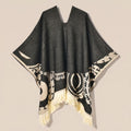 Poncho femme ethnique noir et crème à franges présenté à plat, vue de face, détaillant le col en V, les motifs et les franges