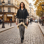 Poncho femme ethnique noir et crème à franges porté par une femme marchant de face sur une rue pavée, montrant son ampleur