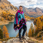 Poncho mexicain homme à capuche, coloris fuchsia, bleu et noir, porté de face par un homme près d'un lac