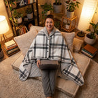 Poncho plaid à carreaux blancs porté par une femme souriante assise sur des coussins avec un ordinateur portable.