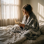 Poncho plaid à carreaux gris, porté par une femme lisant un livre confortablement installée dans son lit.