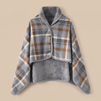 Poncho plaid à carreaux gris et brun présenté à plat, montrant le motif et la doublure douce.