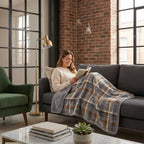 Poncho plaid à carreaux gris et brun utilisé comme couverture par une femme lisant sur un canapé.