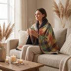 Poncho plaid à carreaux multicolores, porté par une femme assise sur un canapé avec une boisson chaude.