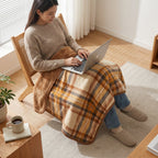 Poncho plaid à carreaux ocre drapé sur les jambes d'une femme assise utilisant un ordinateur portable.