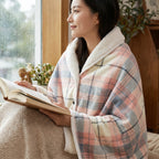 Poncho plaid à carreaux pastel porté par une femme lisant un livre près d'une fenêtre lumineuse.