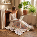 Poncho plaid à carreaux pastel utilisé comme couverture par une femme travaillant sur un ordinateur portable au sol.