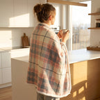 Poncho plaid à carreaux pastel vu de dos sur une femme tenant une tasse dans une cuisine moderne et lumineuse.