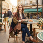 Poncho plaid colorblock camel porté par une femme assise à la terrasse d'un café, buvant un café.