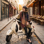 Poncho plaid colorblock camel porté par une femme assise sur un scooter vintage dans une ruelle pavée.