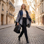 Poncho plaid colorblock gris porté par une femme souriante marchant sur une rue pavée.